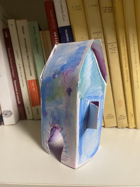 Piccola casa in cartoncino dipinta ad acquerello, su una libreria